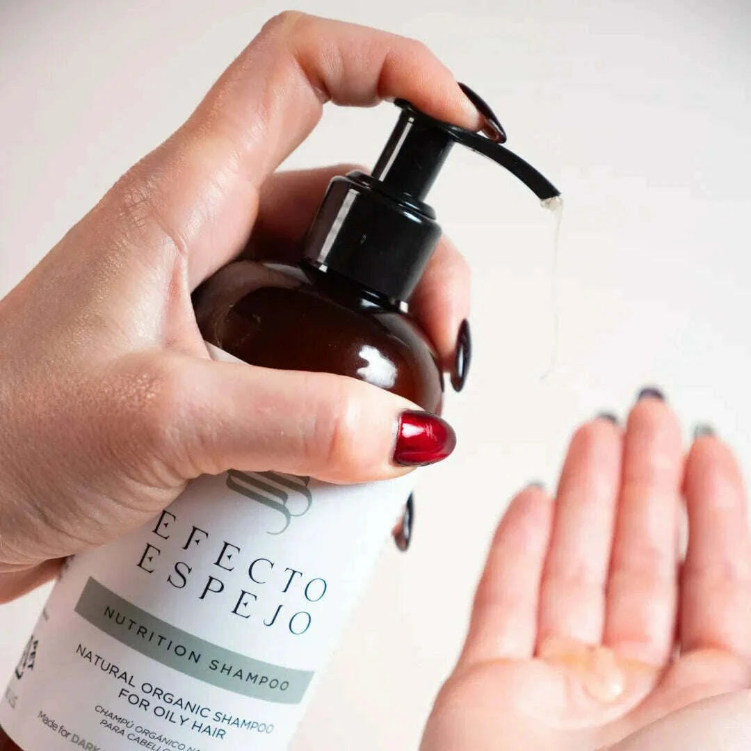 Hand holding a bottle of Efecto Espejo Nutritive Shampoo for Oily Dark Hair, pouring a small amount onto the other hand.