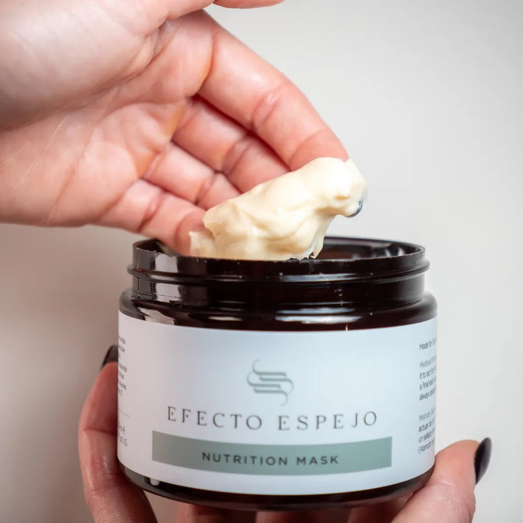 Hand holding an open jar of Efecto Espejo Nutritive Hair Mask for Oily Dark Hair, with the other hand showing a portion of the product scooped out.